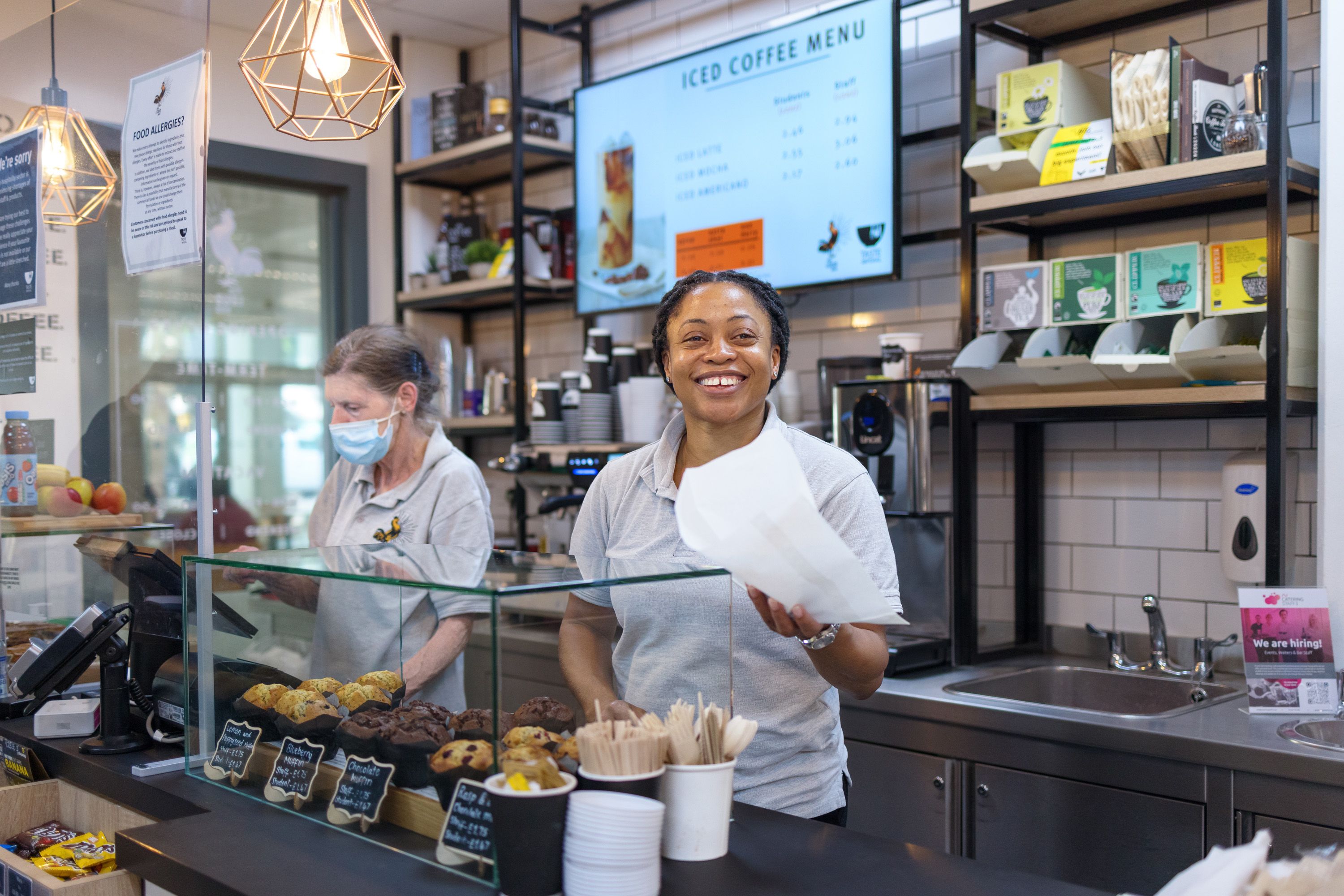 Member of catering staff Pauline King behind the counter in an Imperial coffee shop, proffering a pastry