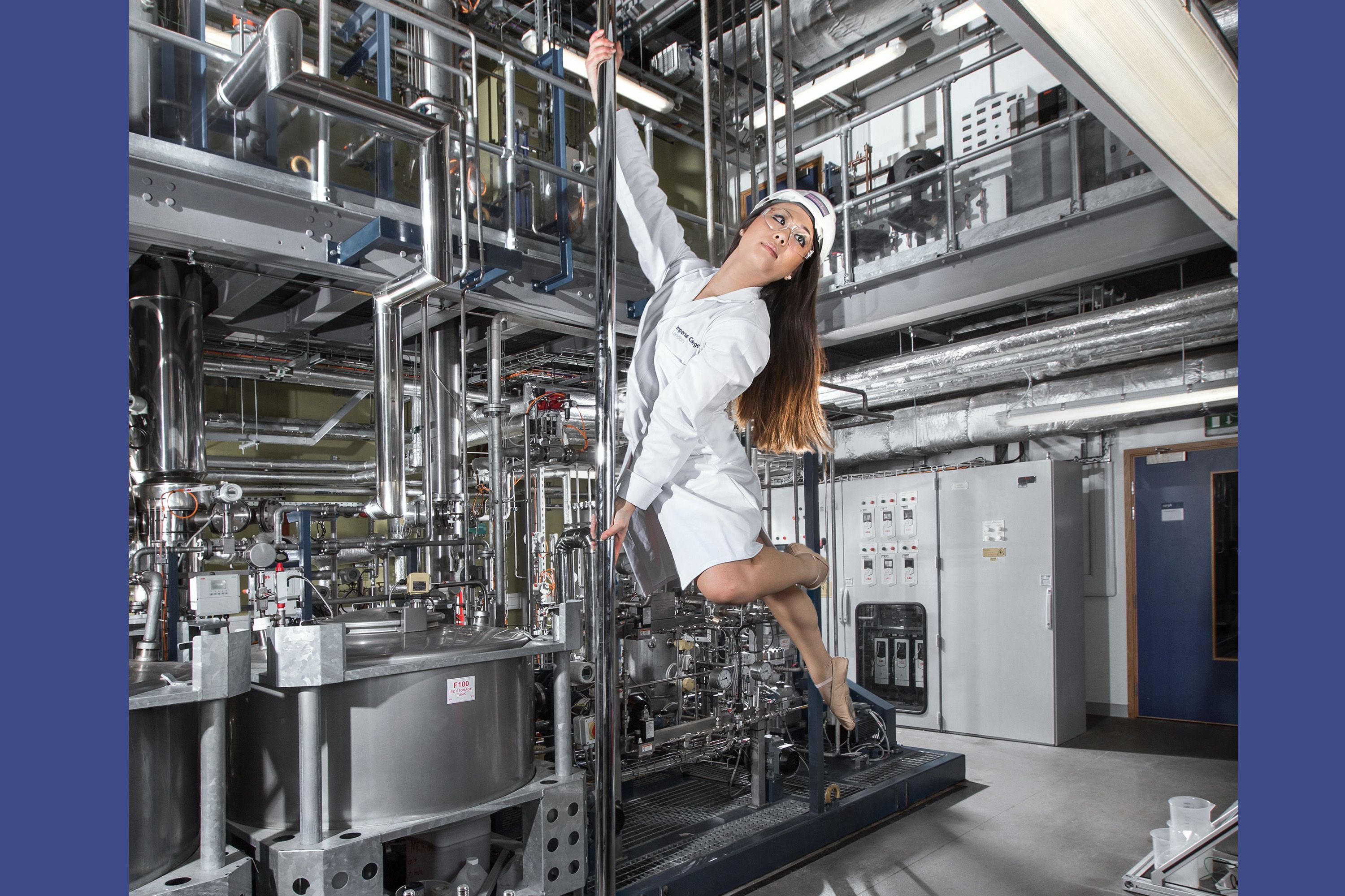 A female student wearing a lab coat and protective headwear hanging from a pole in an engineering lab