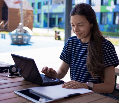 Woman sits on her laptop at an outside table with a coffee