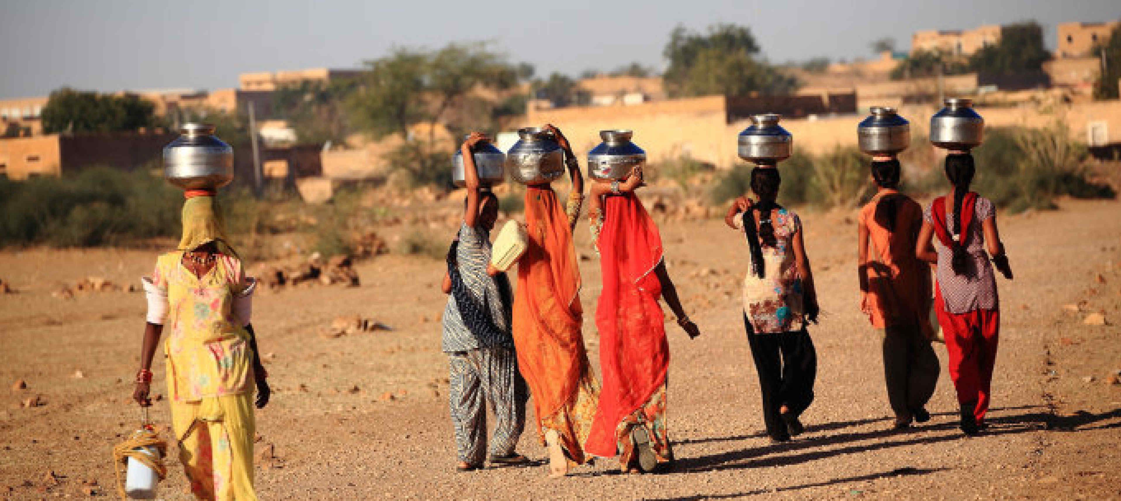 women in India walking away from the camera with water pots on their head