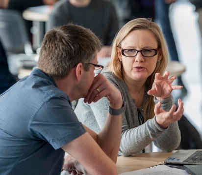 a man and a woman talking while sat in front of a laptop