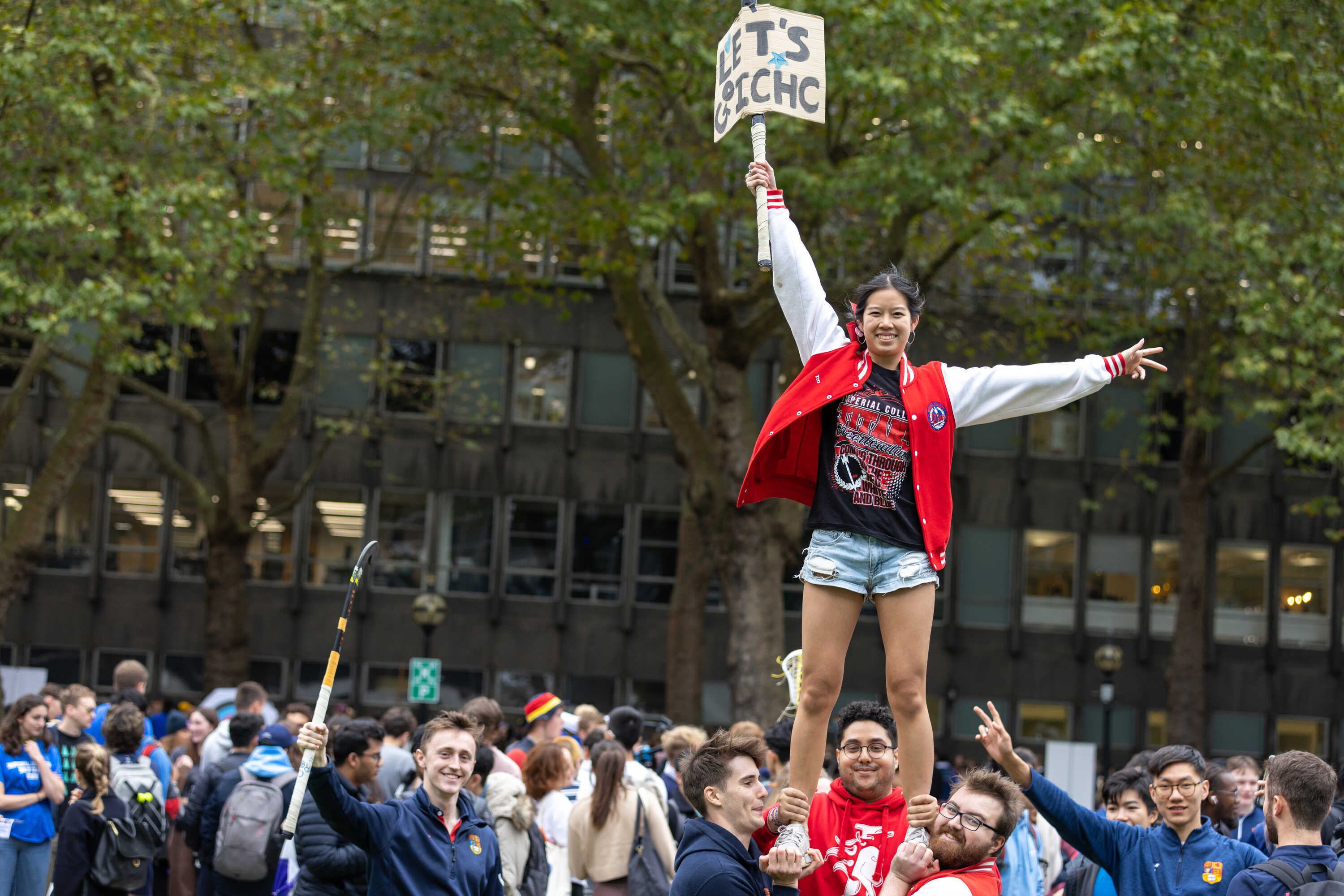 Student being lifted up holding sign at student societies fair