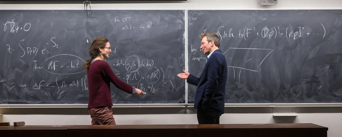 Two people discussing theoretical physics in front of a blackboard