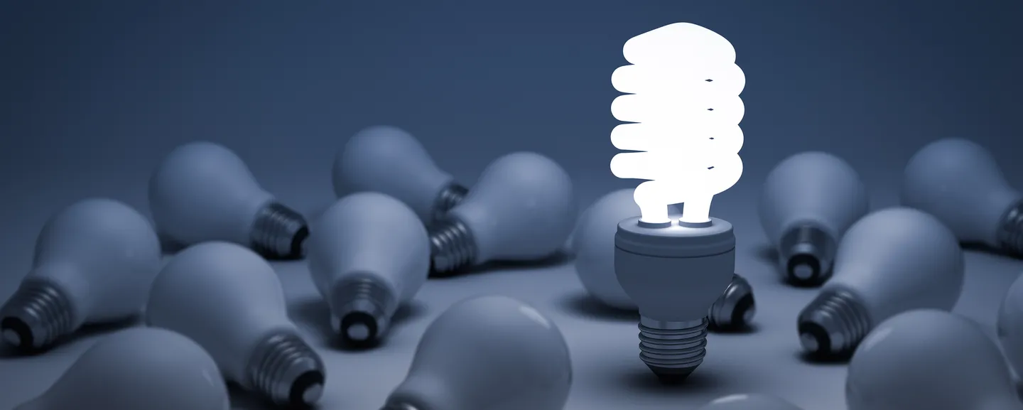 Glowing energy efficient lightbulb surrounded by old-style lightbulbs