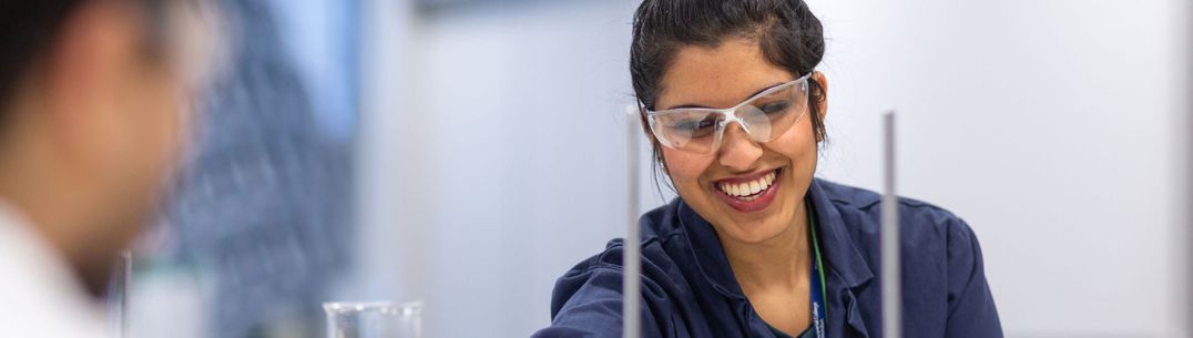 A researcher wearing a lab coat and safety glasses adjusts a piece of equipment in a lab