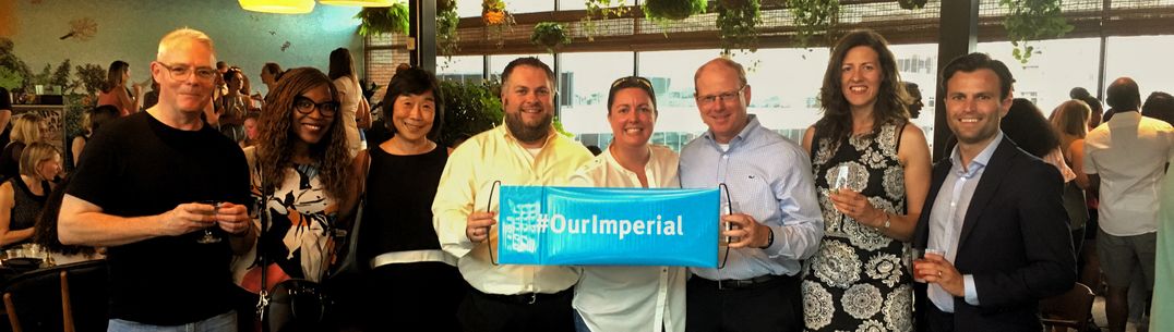 Group  of alumni at an event holding a sign saying #OurImperial