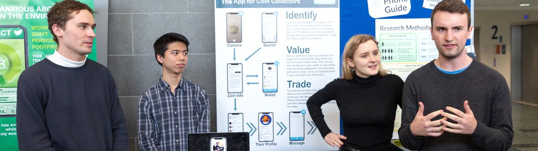 Four students standing in front of exhibition boards delivering a presentation