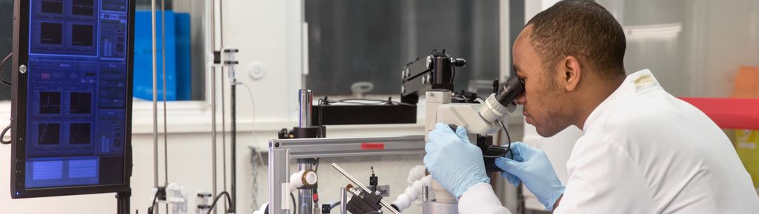 A bioengineering researcher wearing a lab coat and looking through a microscope 