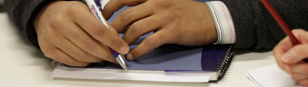 Hand holding a pen and resting on a notebook