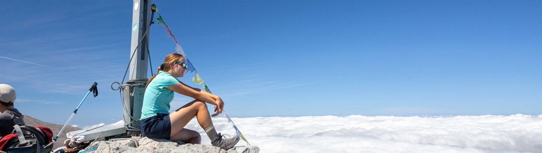 A student sitting on top of a mountain looking out over clouds