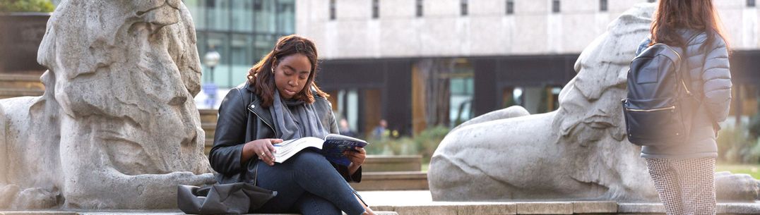 A student sits at the base of a stone lion and reads from a textbook