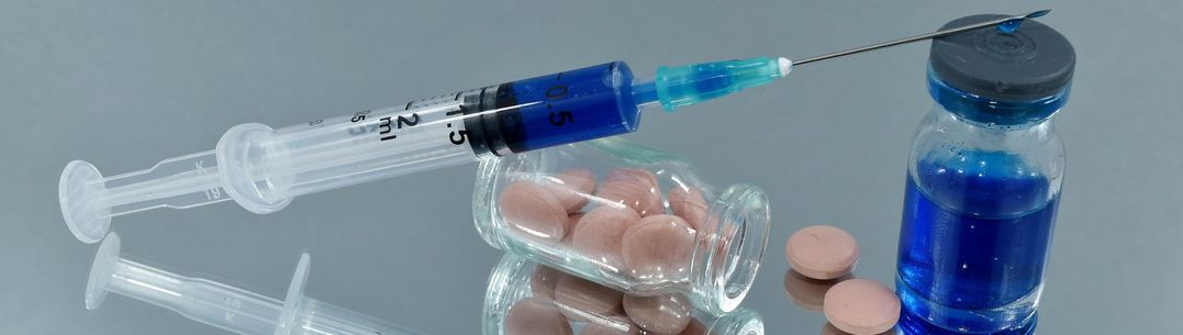 A syringe of blue liquid and a glass vial of pink tablets on a mirror