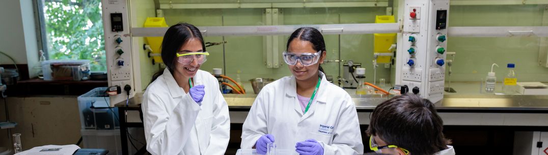 Three students in a wet lab wearing lab coats, safety glasses and gloves