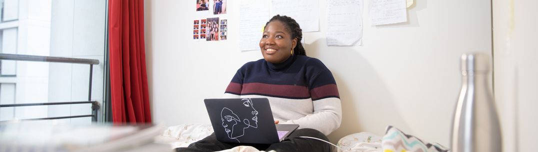 A student sitting on a bed with a laptop in College accommodation