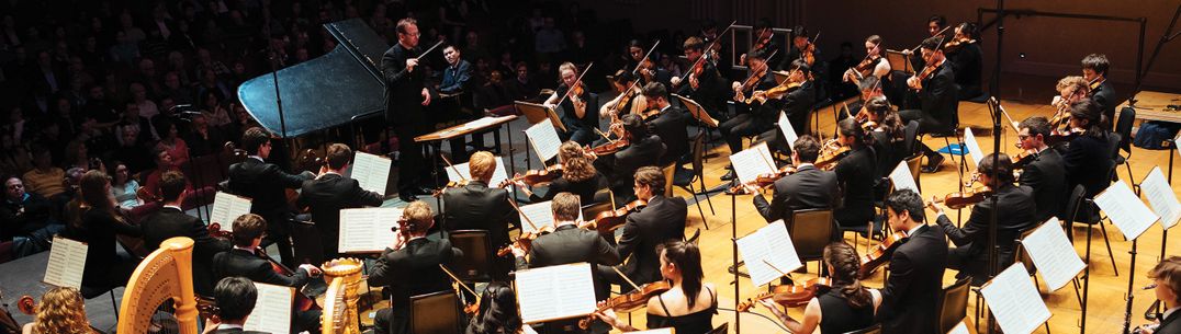 An orchestra in concert are playing at looking at a conductor