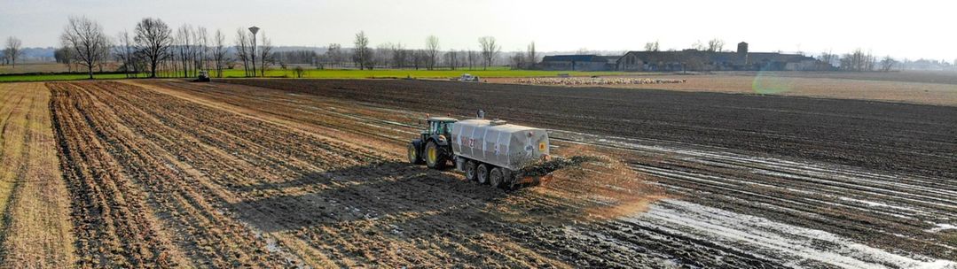 A tractor driving up a field pulling a trailer which is spraying biosolids (manure or treated sewage waste) on a field