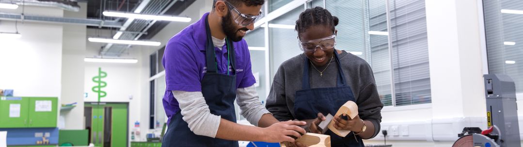 A student and tutor smiling at a work bench.