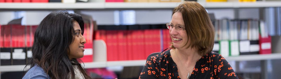 A teacher and a student talking while sitting at a desk with an open book