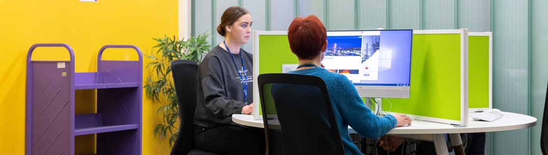 Students sitting at desks in the library, working on a computer
