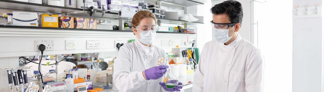 Two researcher in lab coats discuss a sample in a lab