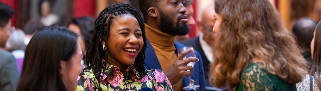 A woman smiles and talks to a group of people while holding a wine glass at an event