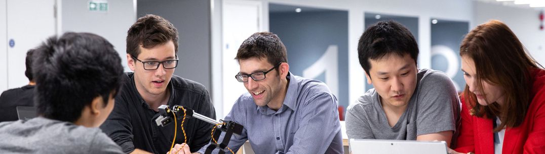 A group of students and a lecturer working on a robotic arm during a class