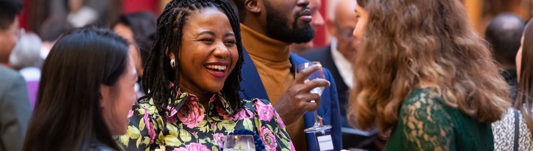 A group of alumni laughing and chatting over drinks at a standing reception