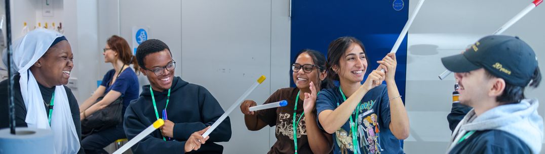 Five smiling students holding up the rockets they have made like light sabers