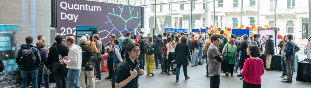 A crowd of people gathering around quantum science demo stands in the Main Entrance to Imperial College London. A banner with Quantum Day 2024 is in the background.