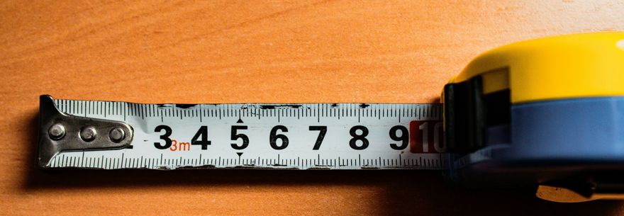 A close up of a white tape measure being extended against a bright orange background