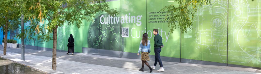 Two people walking in front of a green sign that says cultivating curiosity