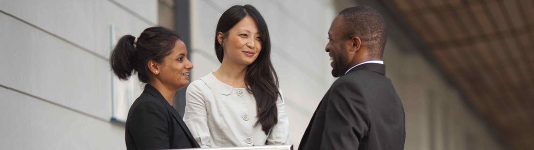 Three people smiling and talking to each other outside