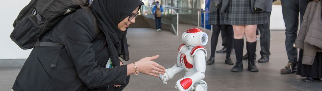 A young woman in a hijab shaking hands with a small humanoid robot