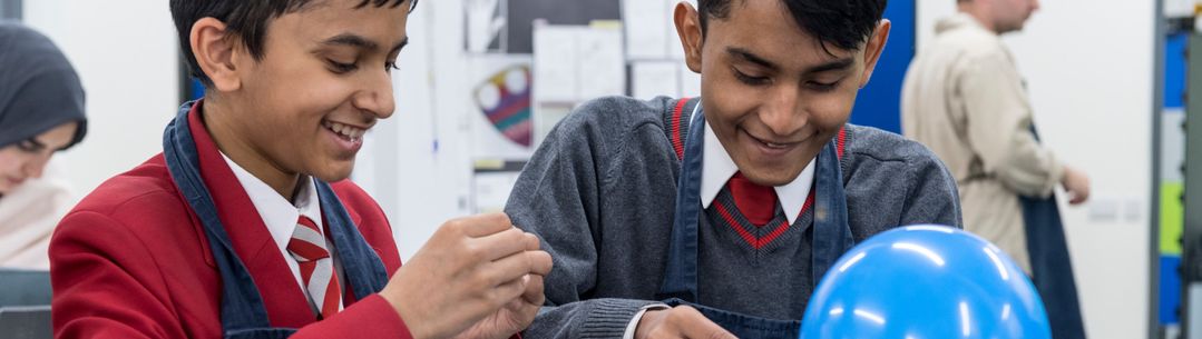 Two young boys smile as they conduct an experiment with a balloon.