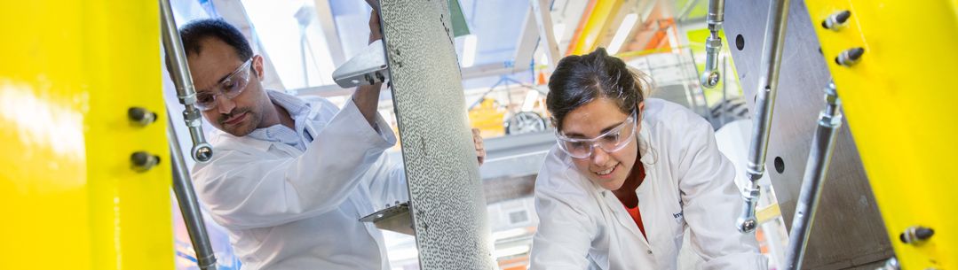 Postdocs in the Dynamic Fracture and Forming Laboratory of the Aeronautics Department testing a yellow panel of aircraft fuselage.