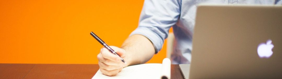 A man writing in notepad and working at a laptop