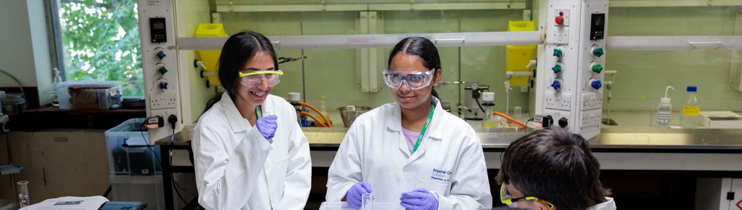 Three students in a wet lab wearing lab coats, safety glasses and gloves