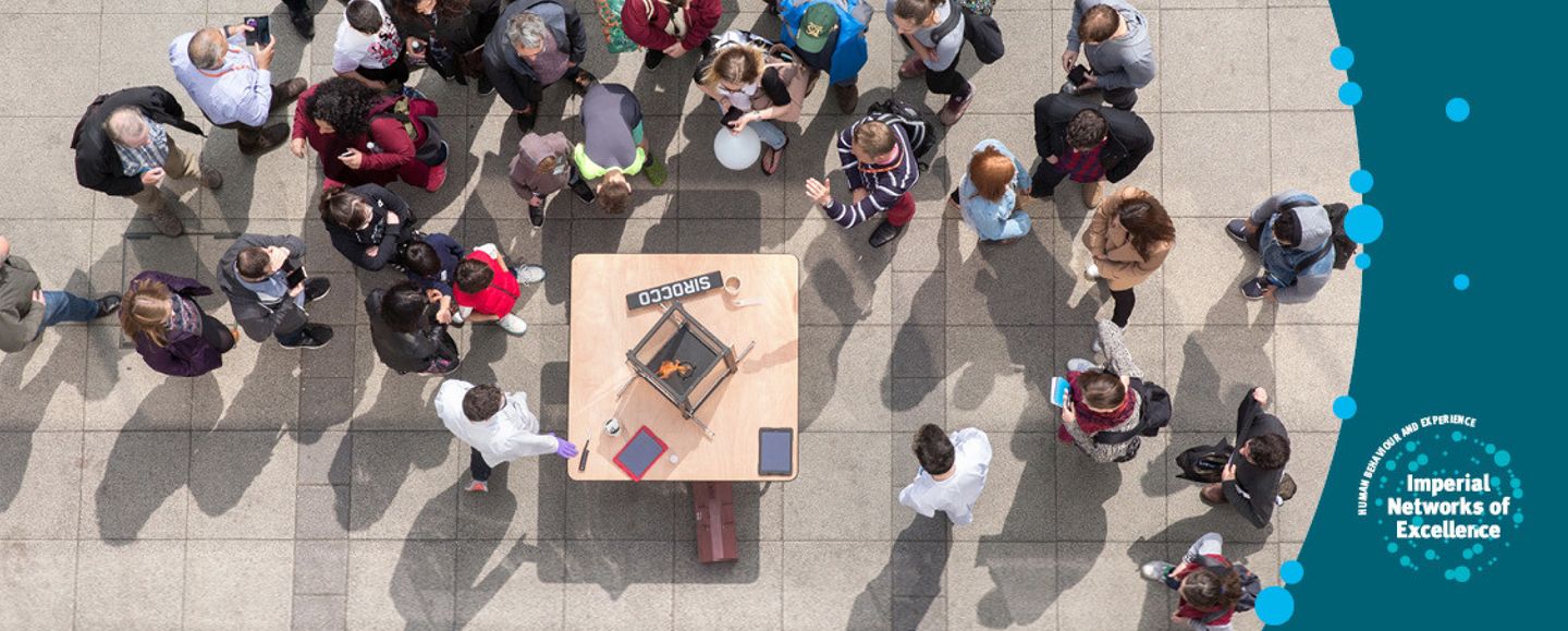 Aerial image of a group of people looking at a box on a table while two scientists demonstrate