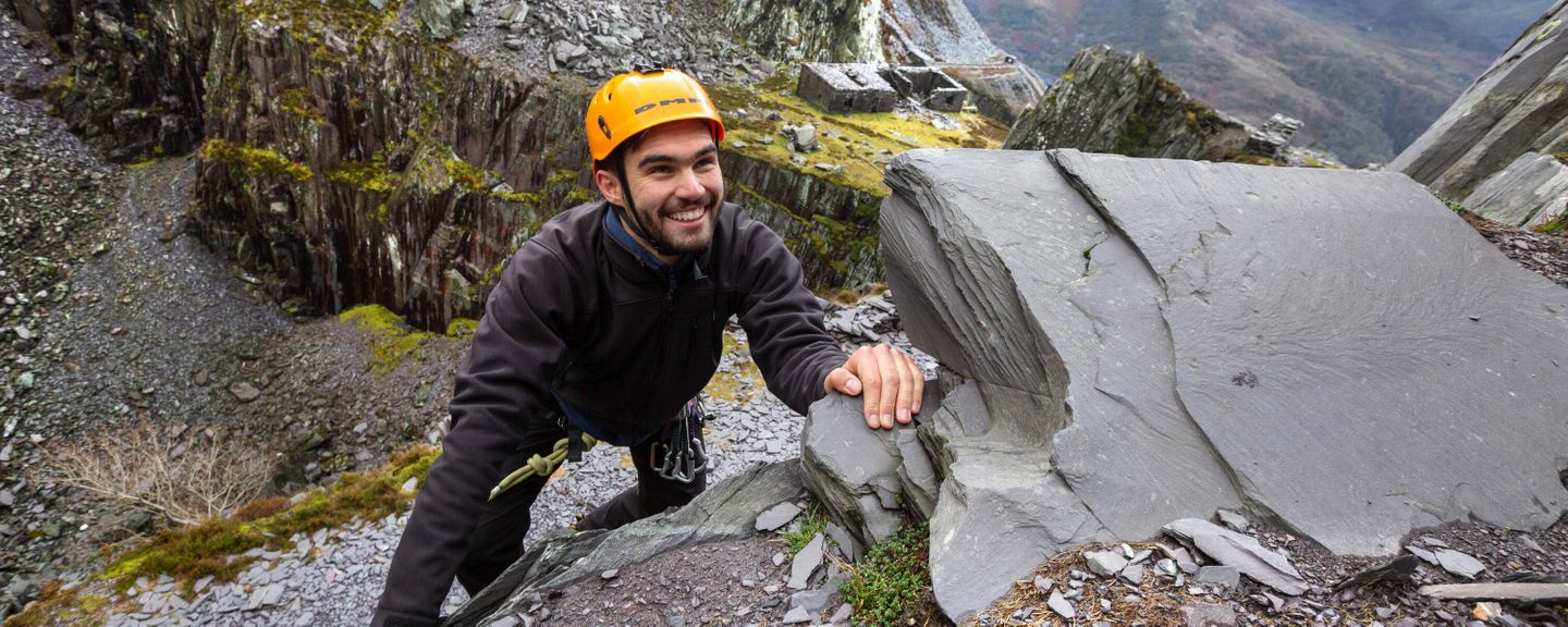 A student climbing a mountain while wearing a helment