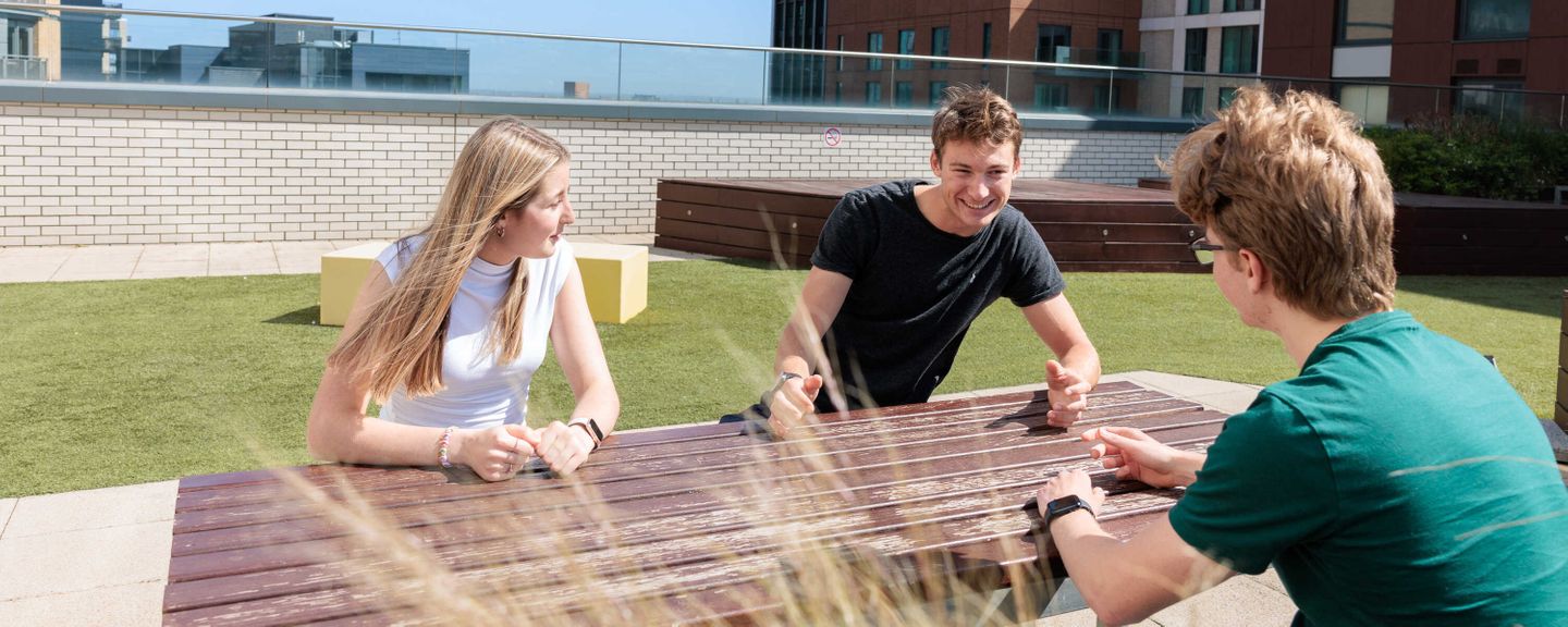 Three students sitting on a bench on a rooftop
