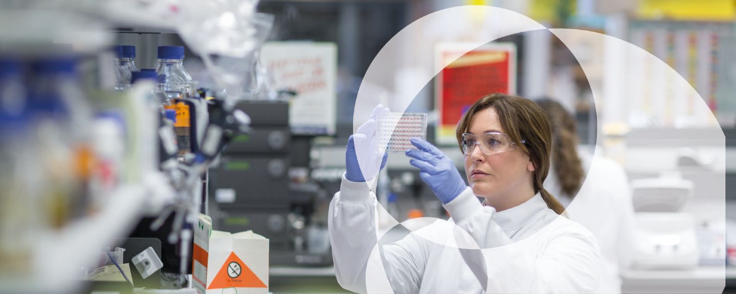 A researcher in a lab coat analyses a multiwell plate