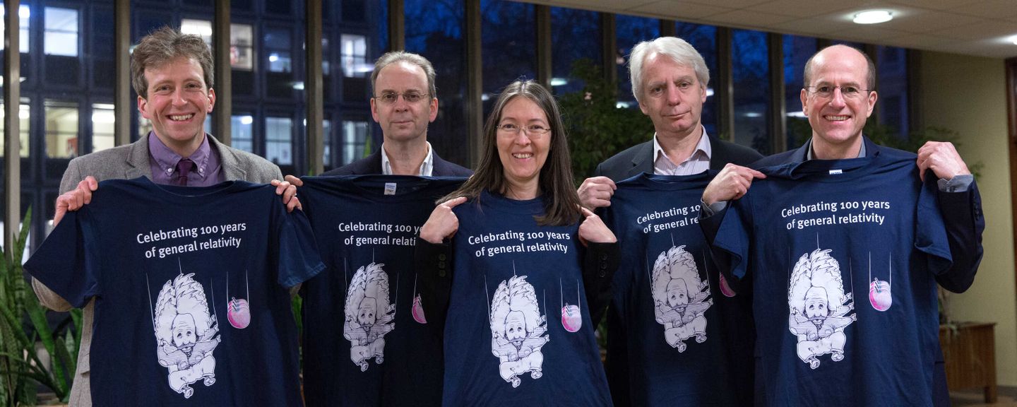 Five theoretical physicists holding up t-shirts