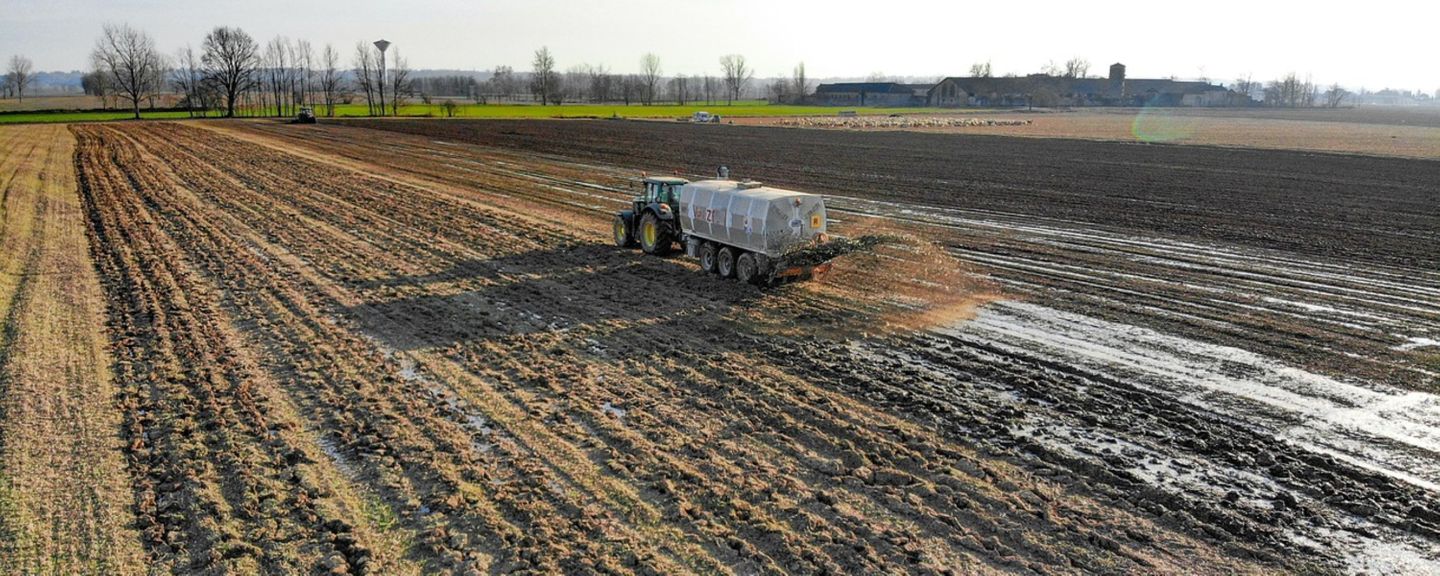 A tractor driving up a field pulling a trailer which is spraying biosolids (manure or treated sewage waste) on a field