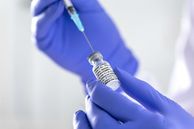 An image of a gloved hand loading a syringe with covid vaccine