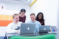 Four students looking at two laptops on a table