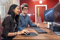 Two students sat at a desk looking at a computer screen