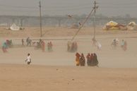 Groups of people in huddles on the dusty bank of Sangam