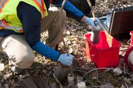 person in field gear collecting sample from pipes in the ground