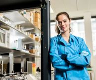 Woman leaning on a fumehood in lab with lab coat on