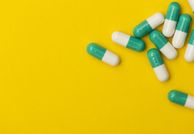 Green and white capsule pills against a yellow background